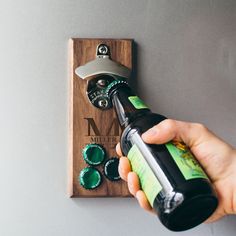 a person holding a bottle opener over a wooden plaque with green glass bottles on it