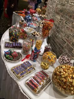 a table topped with lots of candy and candies next to a brick wall in the background