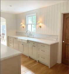 a large kitchen with white cabinets and wood flooring, along with a window over the sink