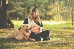 a pregnant woman sitting in the grass with her dog next to her and holding her belly