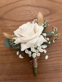 a white rose and baby's breath boutonniere on a wooden table