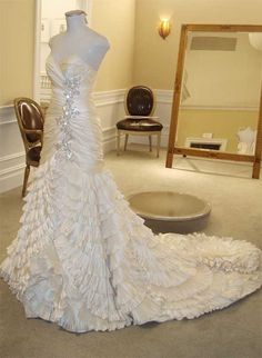 a white wedding dress is on display in a room with chairs and mirror behind it