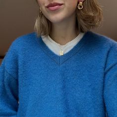 a woman wearing a blue sweater and gold earrings