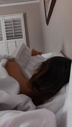 a woman laying in bed reading a book