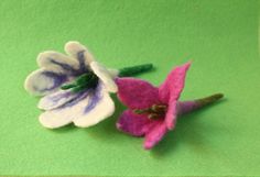 two small felt flowers sitting on top of a green cloth covered surface, one is purple and the other is white