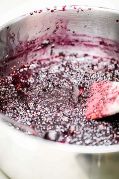 a metal bowl filled with blueberry sauce on top of a stove burner next to a wooden spoon