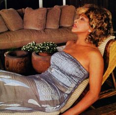 a woman laying on top of a wooden floor next to a couch and flower pot