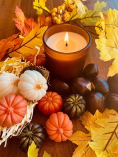 a lit candle surrounded by autumn leaves and acorns on a wooden table with pumpkins