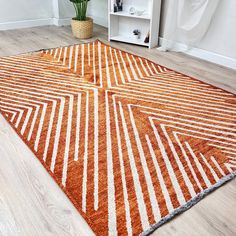 an orange and white area rug on the floor in a living room with a potted plant