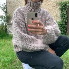 a woman sitting in the grass with her cell phone up to her ear and wearing a turtle neck sweater