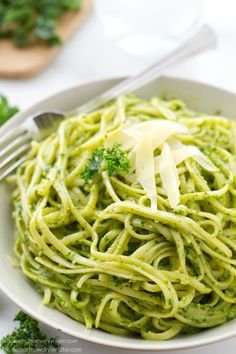 a white bowl filled with green pasta and broccoli on top of a table