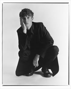 a black and white photo of a man in a suit kneeling down with his hand on his face