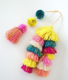 multicolored tassels and pom - poms hanging from string on white surface