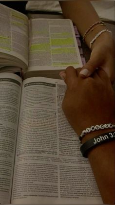 two people holding hands over an open book with the word john written on it and bracelets around their wrists