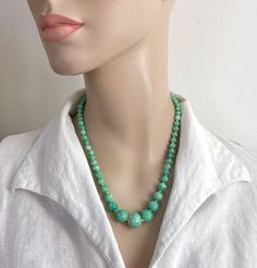 Mid length green Peking glass necklace.  Smooth graduated beads with speckles. Hand knotted on green bead string.  Glass in excellent vintage condition.  Clasp works well.   Minor signs of use and age can be expected.  Ready to wear or gift.  Largest bead is 1.7cm width.  Weight: 39.2g Presented in a gift pouch and sent secured within recyclable packaging. All shop stock is vintage or antique and may show signs of pre-use and wear and is sold as seen. Please check photos for further information Green Gemstone Beaded Necklaces, Green Beaded Emerald Necklace With Round Beads, Vintage Green Beaded Necklaces With Round Beads, Green Vintage Jewelry With Gemstone Beads, Green Gemstone Beads Necklace, Adjustable Green Turquoise Necklace With Round Beads, Green Beaded Emerald Necklace, Green Turquoise Necklace With Round Beads In Vintage Style, Green Turquoise Necklace With Faceted Beads As Gift