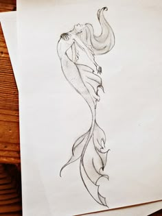 a drawing of a mermaid with her tail curled up in the air, sitting on top of two sheets of paper