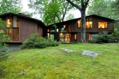 a large brown house sitting on top of a lush green field next to a forest