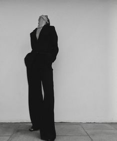 a woman in a black suit leaning against a wall with her hands on her head