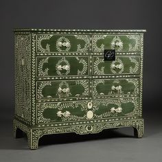 a green and white painted chest of drawers with flowers on the front, decorated with leaves