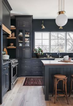 a kitchen with black cabinets and wooden floors, an island countertop and stools