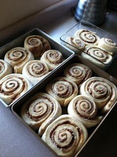 two pans filled with cinnamon rolls sitting on top of a counter