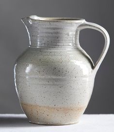 a white vase with brown speckles on the bottom is sitting on a table