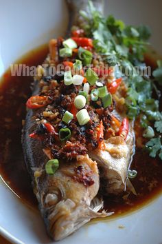 a white plate topped with fish covered in sauce and garnished with cilantro