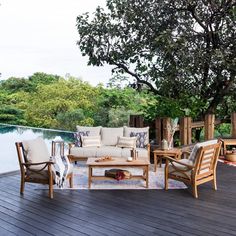 an outdoor living area with wooden furniture and trees in the background, on a deck overlooking a body of water