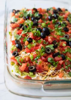 a glass casserole dish filled with black olives, tomatoes and cheese