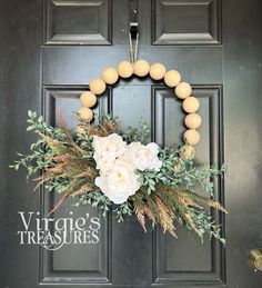 a wreath with white flowers and greenery hangs on the front door of a house