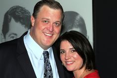 a man in a suit and tie standing next to a woman wearing a red dress