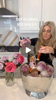 a woman pouring wine into a bowl filled with iceballs and roses in a kitchen