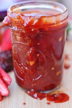 a jar filled with strawberry jam sitting on top of a wooden table next to sliced strawberries