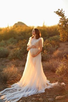 a pregnant woman standing in the desert at sunset with her hands on her belly, wearing a white dress