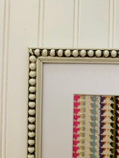 a white frame holding a multicolored striped wallpaper with beaded trim around the edges