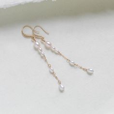 Expertly crafted for the modern bride, these long gold-filled earrings feature genuine pearls and a sleek, handcrafted design. Elevate any ensemble with these timeless, sophisticated accessories. - Handcrafted with genuine freshwater pearls. - Gold filled chain pictured - Gold plated earring wire with CZ stones - Available in gold filled, rose gold filled or rhodium (silver). - Earrings measure 3 inches - Nickel free and hypoallergenic This is an original design by © Treasures by Agnes PLEASE ALLOW APPROX 7 BUSINESS DAYS FOR COMPLETION MATCHING PIECES: https://www.etsy.com/listing/1777474326/pearl-back-necklace-for-wedding-bridal?click_key=736c66cfe217b2bc273a13effc42d9c42fcd5d2e%3A1777474326&click_sum=a139307c&ref=shop_home_active_1&pro=1&frs=1&sts=1 https://www.etsy.com/listing/179165355 14k Gold Filled Pearl White Wedding Earrings, 14k Gold-filled White Linear Long Drop Earrings, White 14k Gold Filled Long Drop Linear Earrings, White 14k Gold Filled Bridal Earrings For Wedding, Gold Dangle Pearl Earrings For Wedding, 14k Gold Filled Dangle Pearl Earrings For Wedding, White Long Drop Pearl Earrings In 14k Gold Filled, White Long Drop Pearl Earrings In 14k Gold, Delicate Wedding Linear Earrings With Pearl Chain