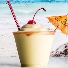 a drink on the beach with an umbrella next to it and some straws sticking out of it