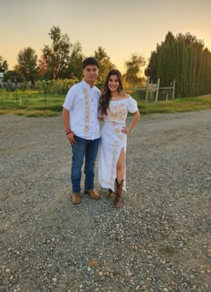 a man and woman standing next to each other on gravel ground with trees in the background