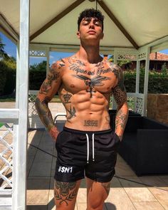 a man with tattoos and no shirt standing in front of a gazebo wearing shorts