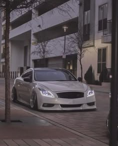 a white car parked on the side of a road next to a tree and building