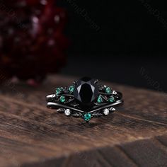 a black diamond ring with green stones on it sitting on top of a wooden table