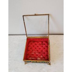 an open box with red fabric inside sitting on a white tablecloth covered floor next to a wall