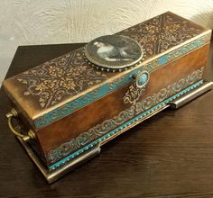 an ornately decorated wooden box sitting on top of a wood table next to a lamp