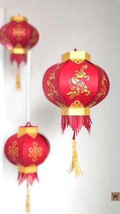 three red paper lanterns with gold designs hanging from the ceiling in a white walled room