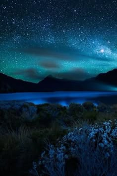 the night sky is filled with stars and bright lights above a body of water surrounded by mountains