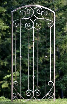 an iron gate in the middle of a grassy area with trees in the back ground