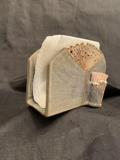 an old book with a fan on it sitting on a black cloth covered tablecloth