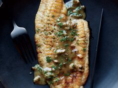 a piece of fish covered in green sauce and garnished with parsley on a plate