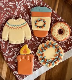 decorated cookies are sitting on a table next to an orange and blue sweater, cupcakes, and donut