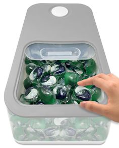 a person is holding a container full of green and white marbles with one hand